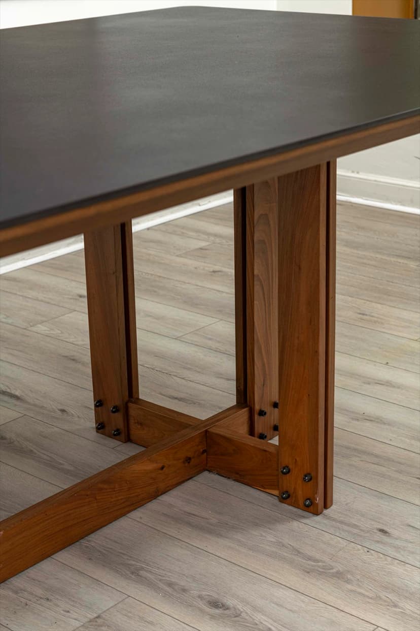 Detalle de mesa de comedor con tapa negra y base de madera maciza en cruz